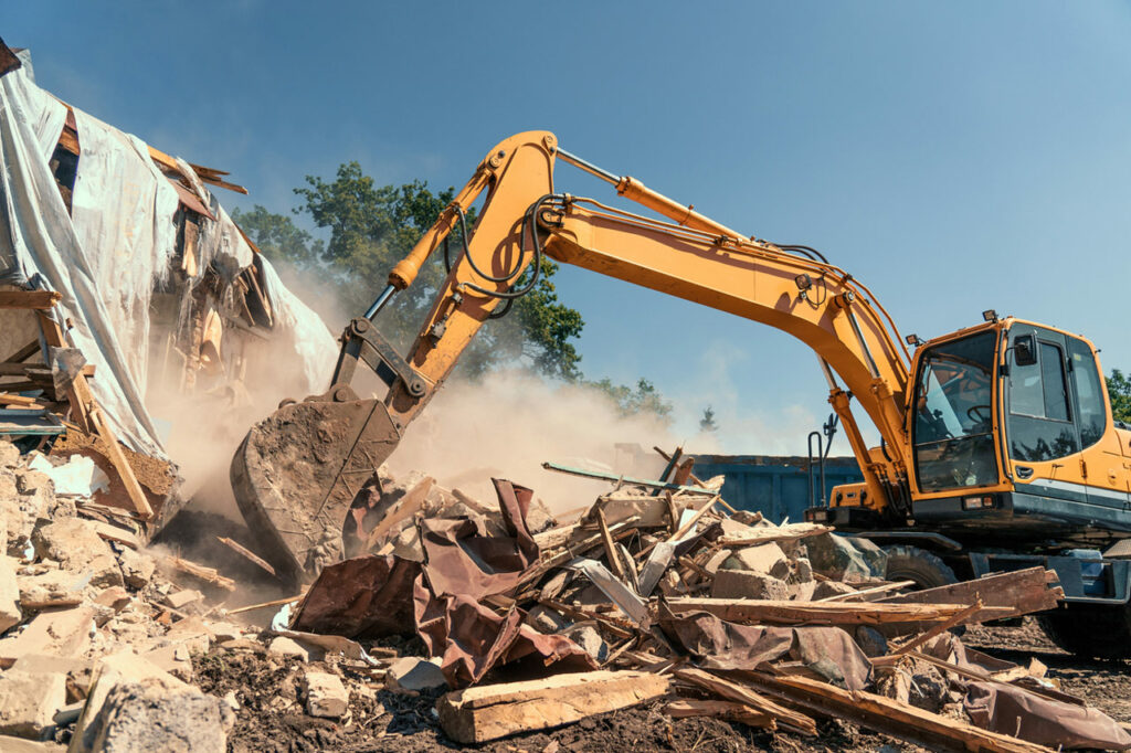 A yellow excavator is demolishing a pile of rubble on a residential property